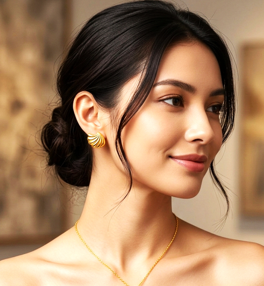 Woman wearing gold jewelry including earrings and a necklace, with a blurred indoor background.