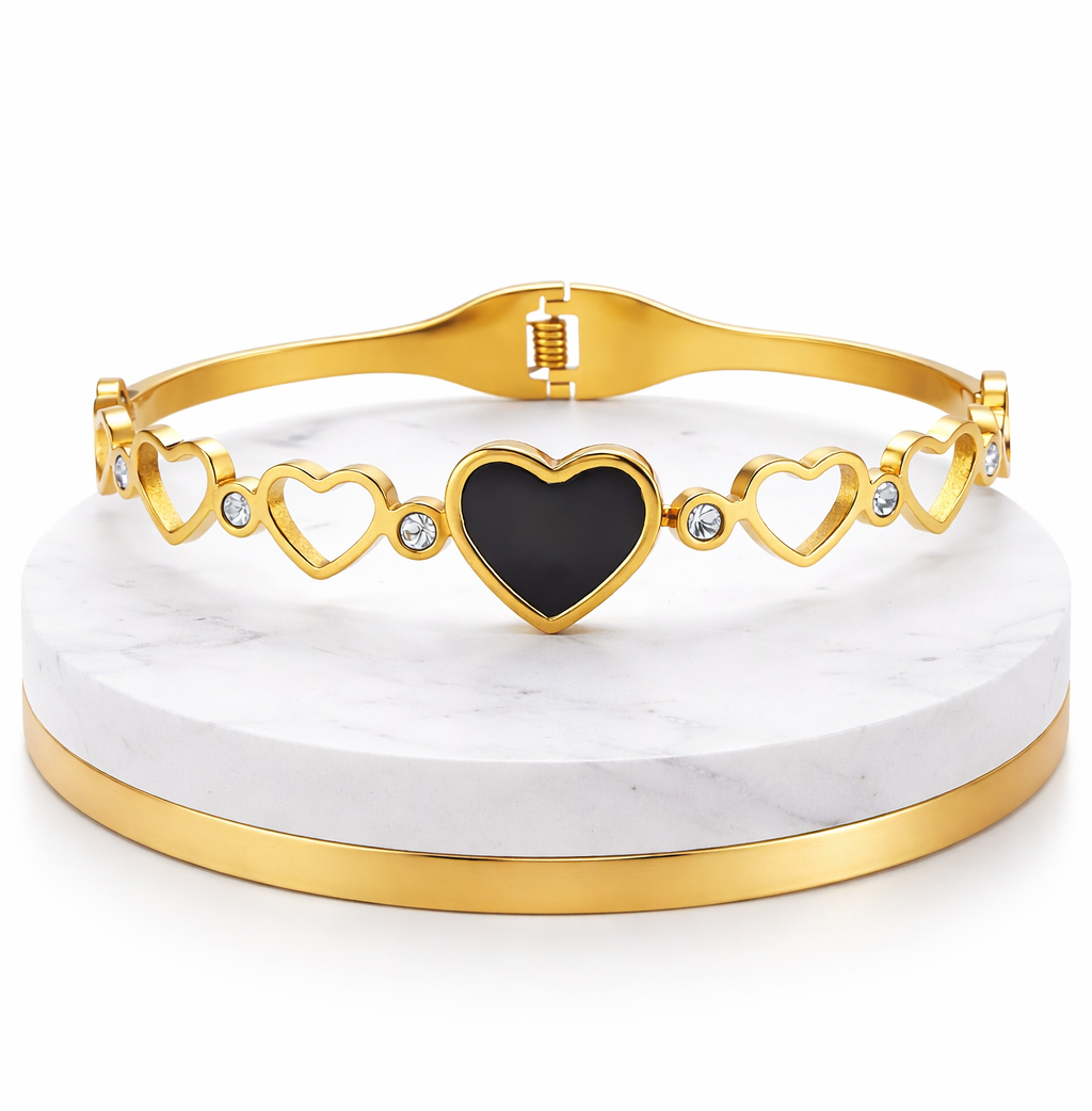 Gold bracelet with a black heart charm on a white marble stand